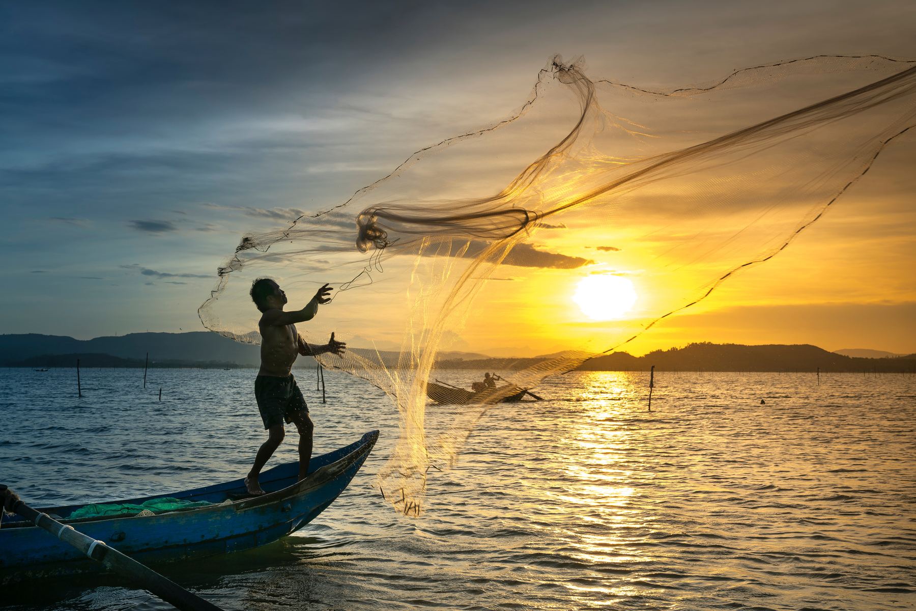 Người đánh cá quăng lưới lúc bình minh trên biển